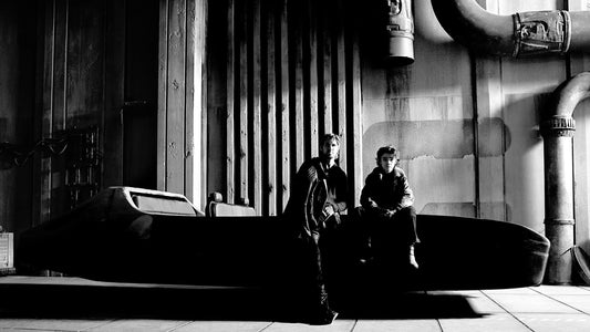 Black and white photo of Ryan Gosling and Flynn Gray sitting on a speeder on the Star Wars: Starfighter set
