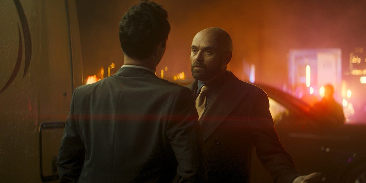 Two men in suits talking under orange light in Clayface