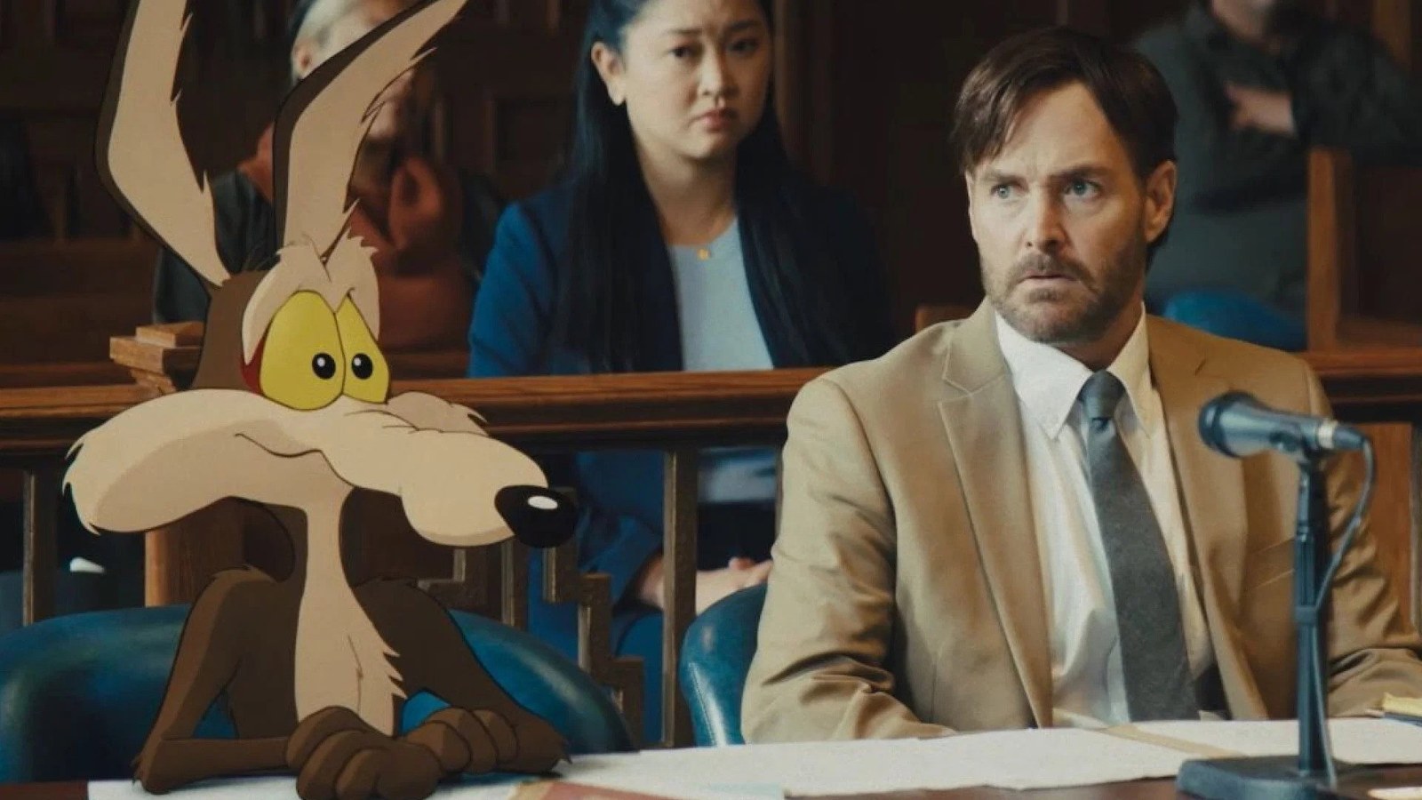 Wile E. Coyote sitting next to Will Forte in a courtroom in Coyote vs. Acme