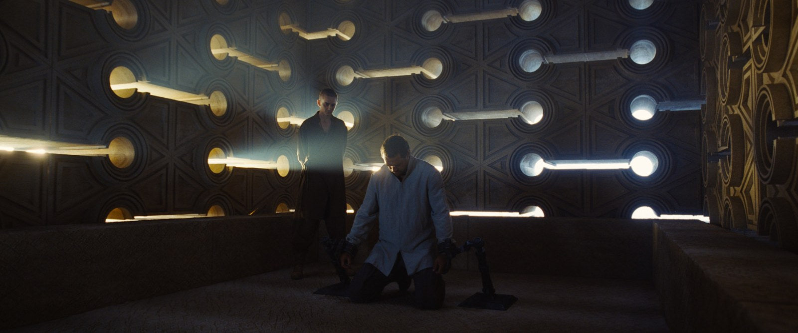 A figure kneeling in a dark chamber lit by beams of light in Dune: Part Three